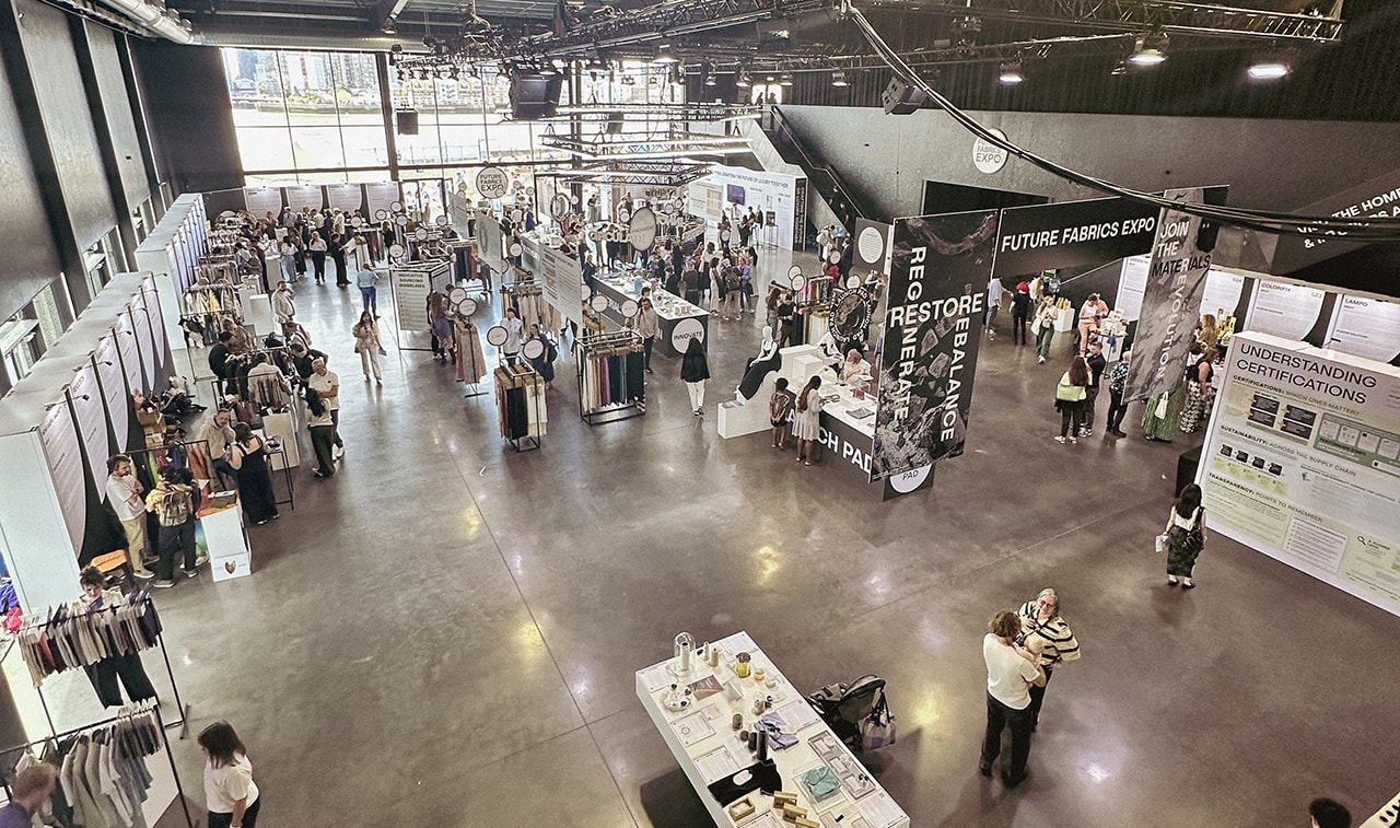 Photo of an aerial view of a sourcing show with various booths, signage and people.
